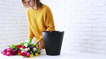 Woman florist dressed in yellow making beautiful bouquet of tulips. front view video