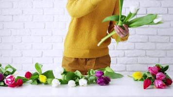 Woman florist dressed in yellow making beautiful bouquet of tulips. front view video