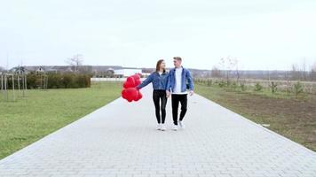 Liebe. Junger Mann umarmt und küsst ein Mädchen im Park mit roten Luftballons video