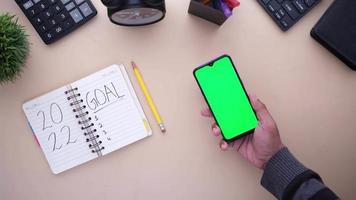 vista superior del teléfono inteligente con pantalla verde y bloc de notas en la mesa. video