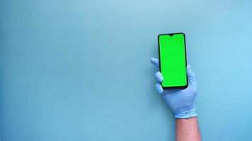 mão em luvas de látex segurando telefone inteligente com tela verde video