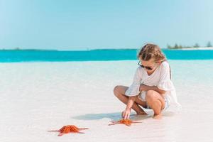 Adorable little girl with starfish on white empty beach photo