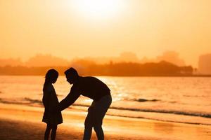 Little girl and dad silhouette in the sunset at the beach photo