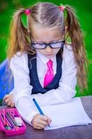 Clever little school girl at desk with notes and pencils outdoor. Back to school. photo