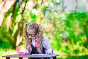 Clever little school girl at desk with notes and pencils outdoor. Back to school. photo
