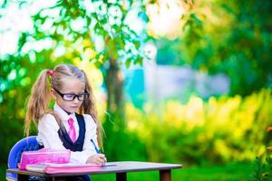 Cute little school girl writing at desk with pencil outdoor. Back to school. photo