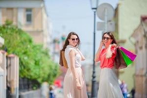 mujeres jóvenes felices con bolsas de compras caminando por la calle de la ciudad. concepto de venta, consumismo y personas. foto