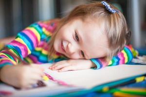 Little cute girl painting with pencils while sitting at her table photo