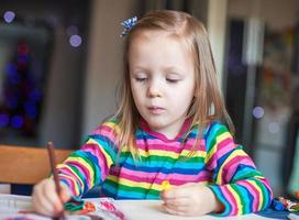 Adorable little girl draws paints sitting at the table photo