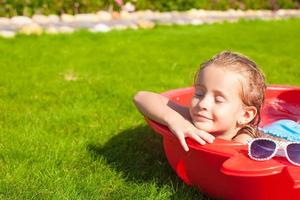 Retrato de relajante adorable niña disfrutando de sus vacaciones en la pequeña piscina al aire libre foto