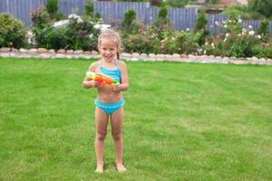 Little adorable girl playing with water gun outdoor in sunny summer day photo