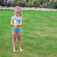 Little adorable girl playing with water gun outdoor in sunny summer day photo