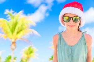adorable niña con sombrero de santa durante las vacaciones navideñas en la playa foto