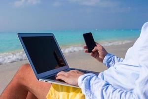 Young man working on laptop at tropical beach photo