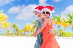 niñas adorables con sombreros de santa durante las vacaciones en la playa se divierten juntas foto