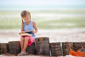 Little adorable girl with book on tropical white beach photo