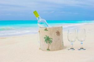 botella de vino blanco y dos copas en la exótica playa de arena foto