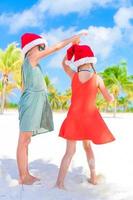 Little adorable girls in Santa hats during beach vacation have fun together photo