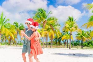 niñas adorables con sombreros de santa durante las vacaciones en la playa se divierten juntas foto