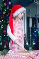 Adorable little girl in Santa hat baking gingerbread Christmas cookies at home photo