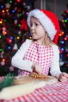 Adorable little girl in Santa hat baking gingerbread Christmas cookies at home photo