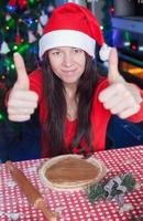 Young woman in Christmas hat raised thumbs up at home photo