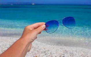Close up of colorful blue sunglasses in hand on tropical beach photo