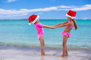 Little cute girls in Santa hats having fun on exotic beach photo