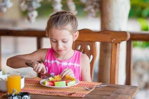 Adorable little girl having breakfast at outdoor cafe photo