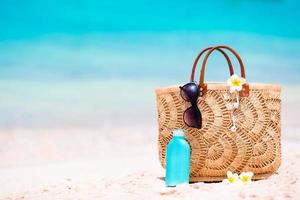 accesorios de playa - bolsa de paja, auriculares, botella de crema y gafas de sol en la playa foto