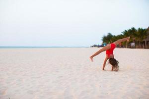 Adorable little girl having fun making cartwheel on tropical white sandy beach photo