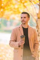 joven bebiendo café con teléfono en el parque de otoño al aire libre foto