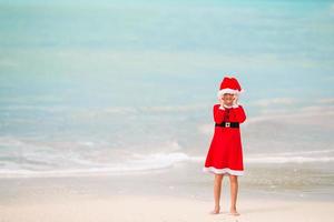 Adorable niña con gorro de Papá Noel en la playa tropical foto