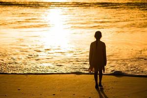 Adorable happy little girl walking on white beach at sunset. photo