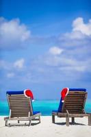 Two loungers with red Santa Hats on tropical beach with white sand and turquoise water photo