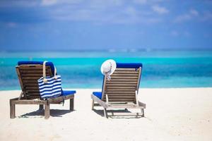 White hat and bag on lounge chairs at tropical sandy beach photo