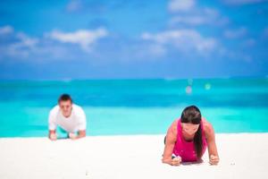 Young fitness couple doing push-ups during outdoor cross training workout on tropical beach photo