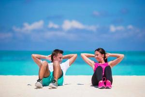 Young fitness couple doing sit ups on white beach photo