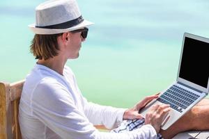 Young man with tablet computer and cell phone on tropical beach photo