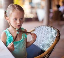 Adorable little girl having breakfast at outdoor cafe photo