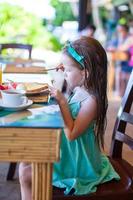 Adorable little girl having breakfast at outdoor cafe photo