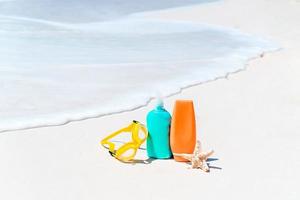 botellas de crema solar, gafas, estrellas de mar y gafas de sol en el océano de fondo de la playa de arena blanca foto