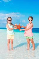 Adorable little girls with starfish on white empty beach photo