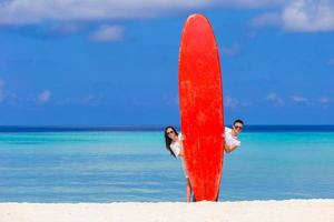 Young couple with red surfboard on white beach photo