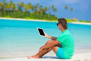 Young man working with laptop at tropical beach photo