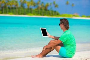 Young man working with laptop at tropical beach photo