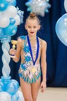 pequeña gimnasta con sus premios deportivos en la alfombra de gimnasia rítmica foto