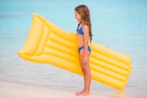 Adorable happy girl with inflatable air mattress on white beach photo