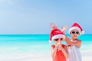 adorables niños pequeños se divierten con sombrero de santa durante las vacaciones navideñas en la playa. año nuevo en la playa foto
