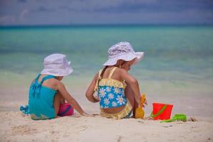 Back view of Two little sisters in nice swimsuits playing on sandy beach photo